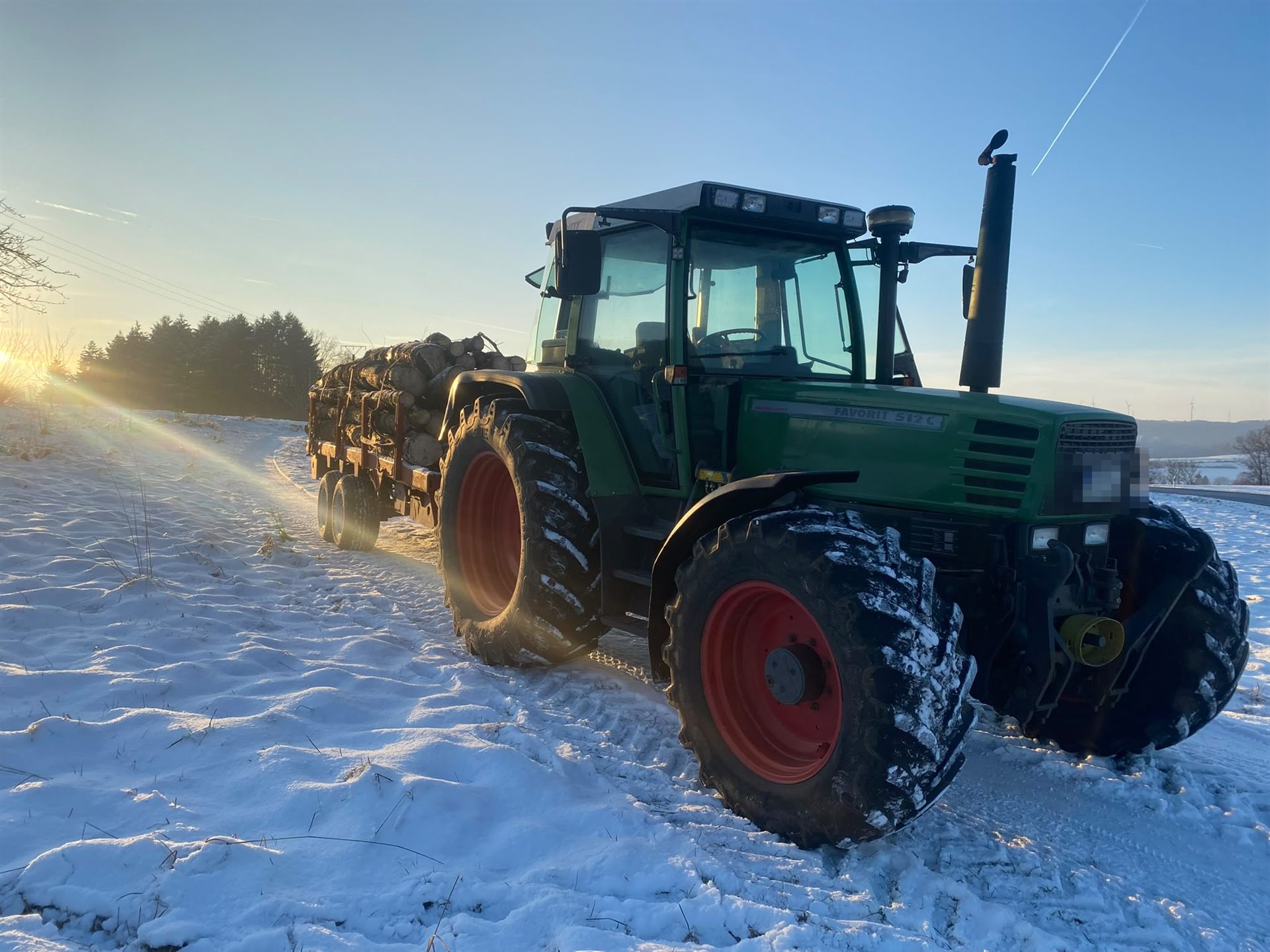 Fendt mit Holzanhänger im Schnee bei Sonnenuntergang